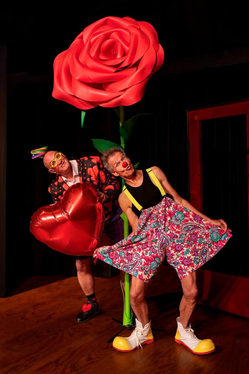 Two people dressed as clowns holding a giant rose