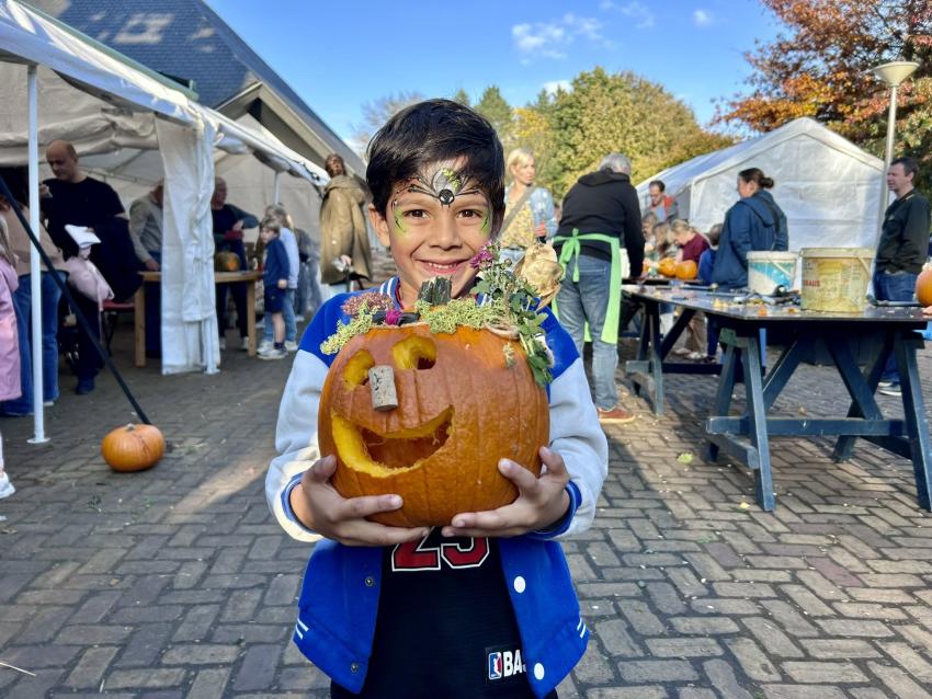 Smiling child with face paint holding a carved pumpkin