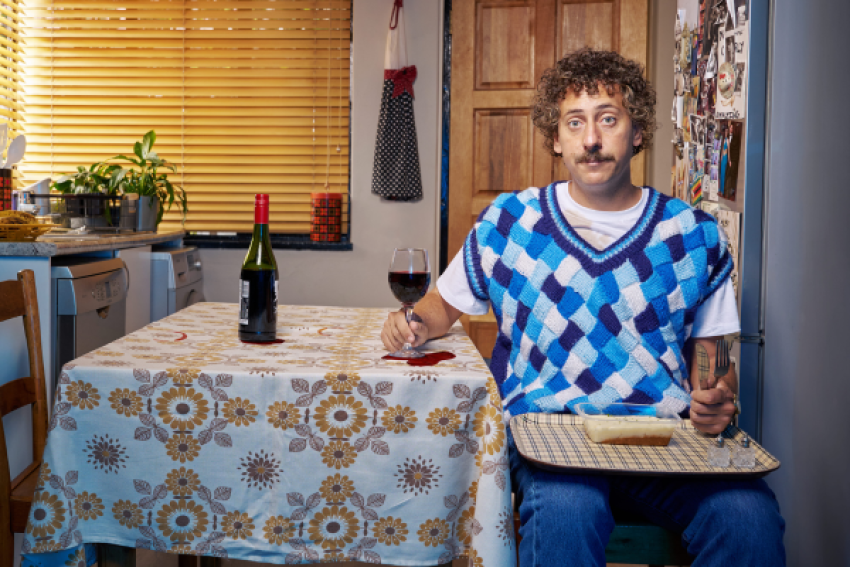 Comedian Schalk Bezuidenhout sitting at a table alone with a glass of red wine