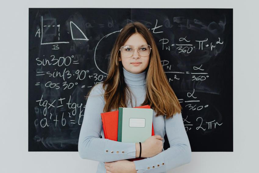 A woman holding books in front of a blackboard with equations
