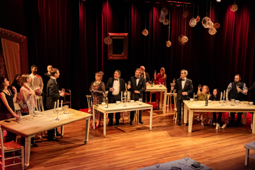 Actors and actresses on stage at a dinner party