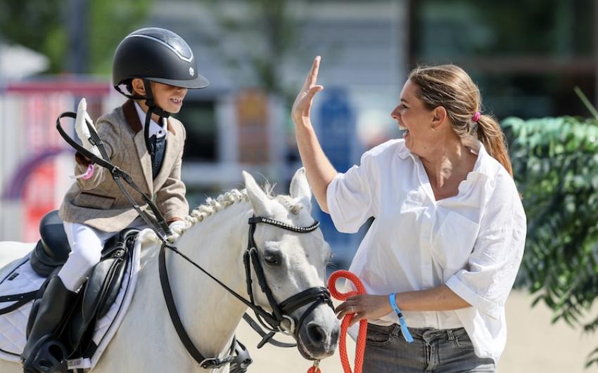 Child on a grey pony high-fiving a smiling woman