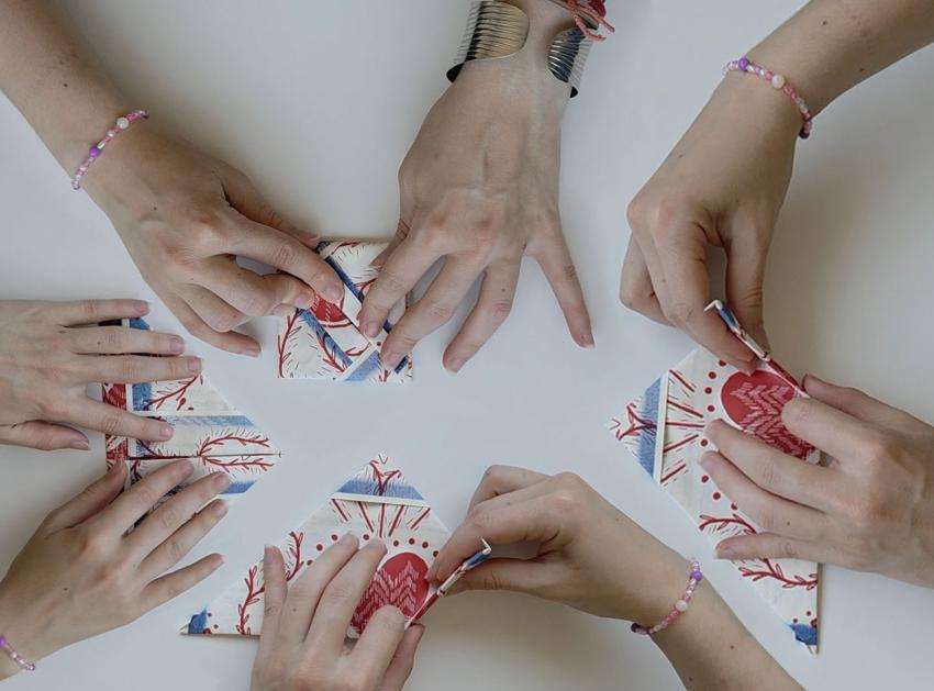 Four pairs of hands folding paper