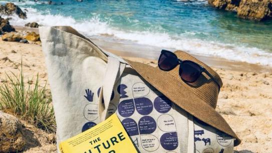 A Praat Nederlands Met Me beach tote bag with hat, sunglasses, and book on a beach, klik voor een vergroting