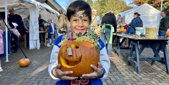 Smiling child with face paint holding a carved pumpkin
