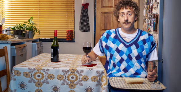 Comedian Schalk Bezuidenhout sitting at a table alone with a glass of red wine