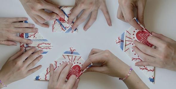 Four pairs of hands folding paper