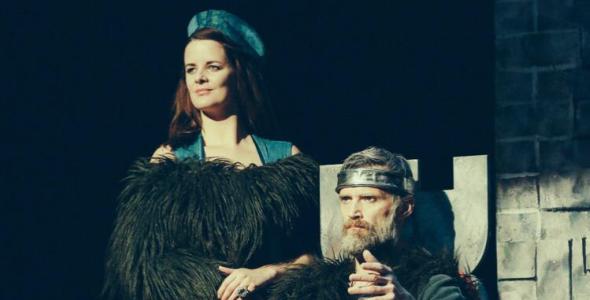 Macbeth sitting on a chair with Lady Macbeth standing beside him